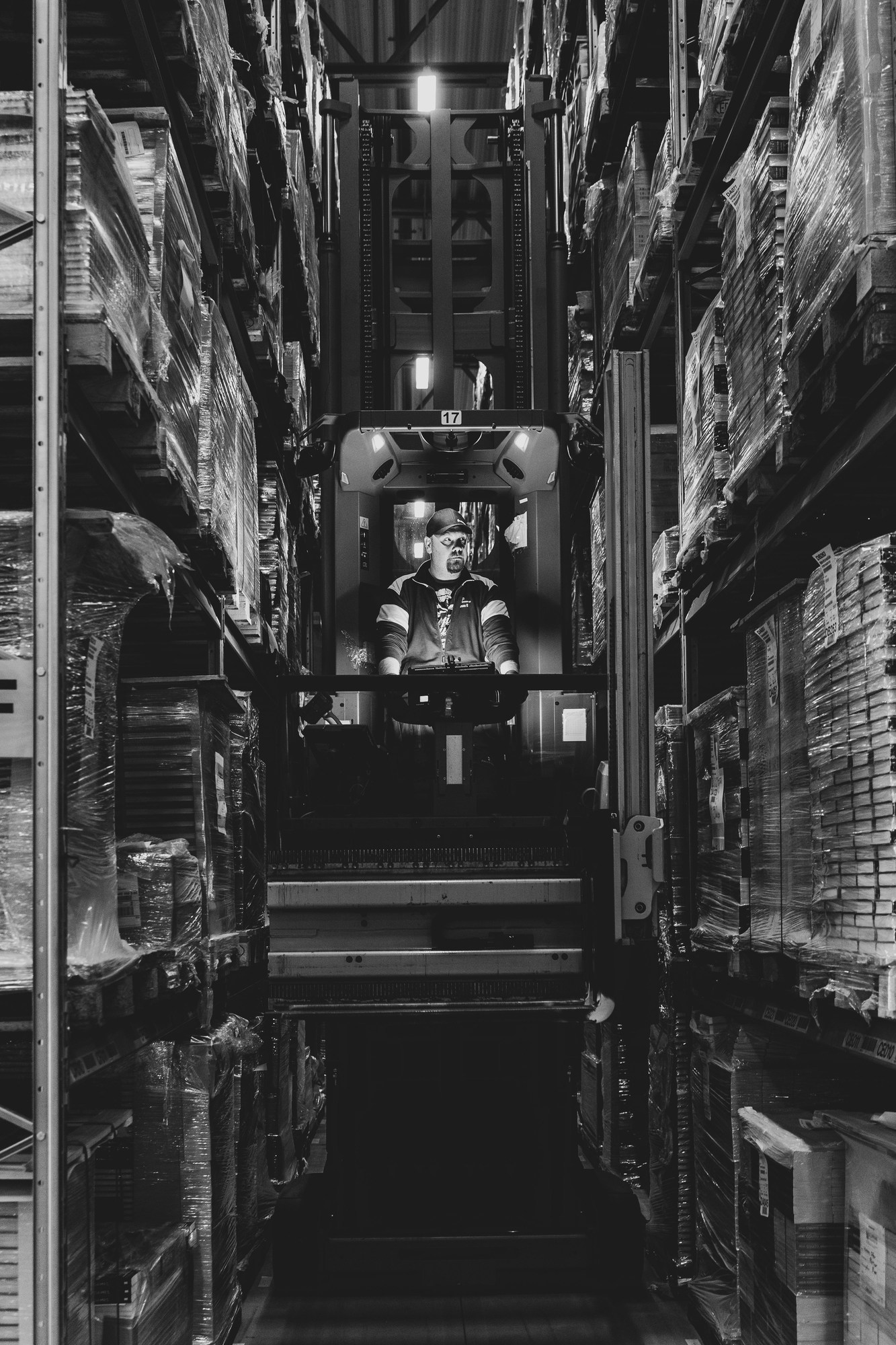 Black-and-white photograph of a reach truck operator between tall pallet storage racks.