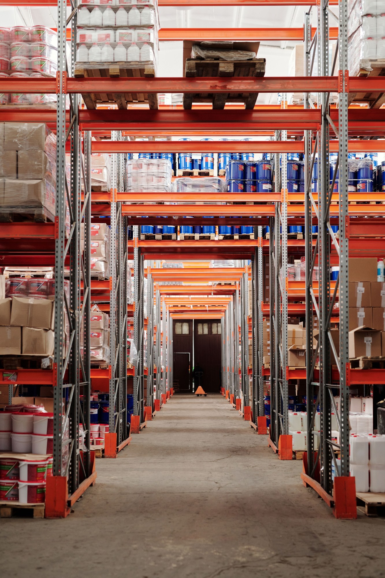 Tall warehouse racks filled with wrapped pallets and cartons along a concrete aisle.